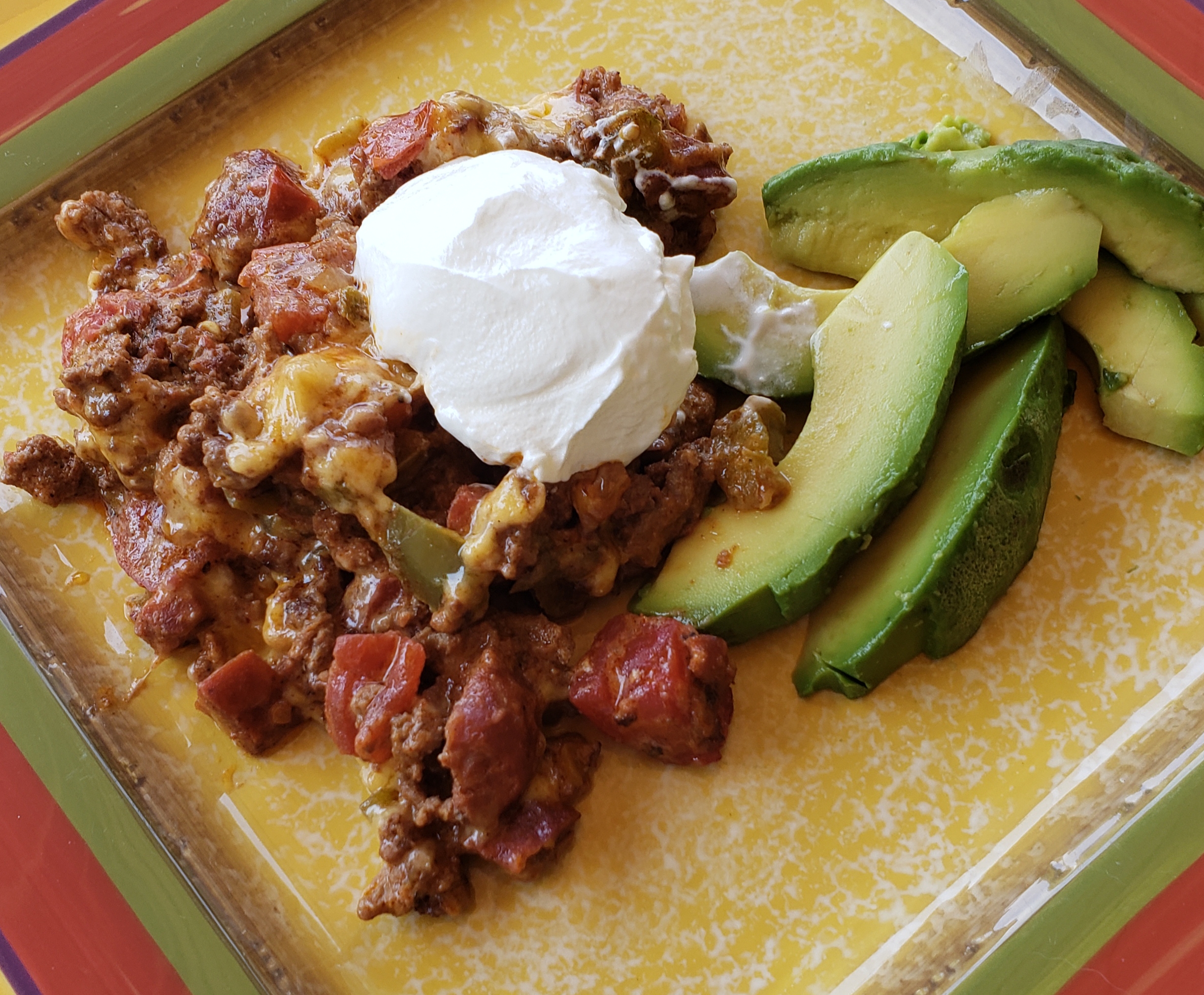 taco casserole on a plate with sour cream and fresh avocado
